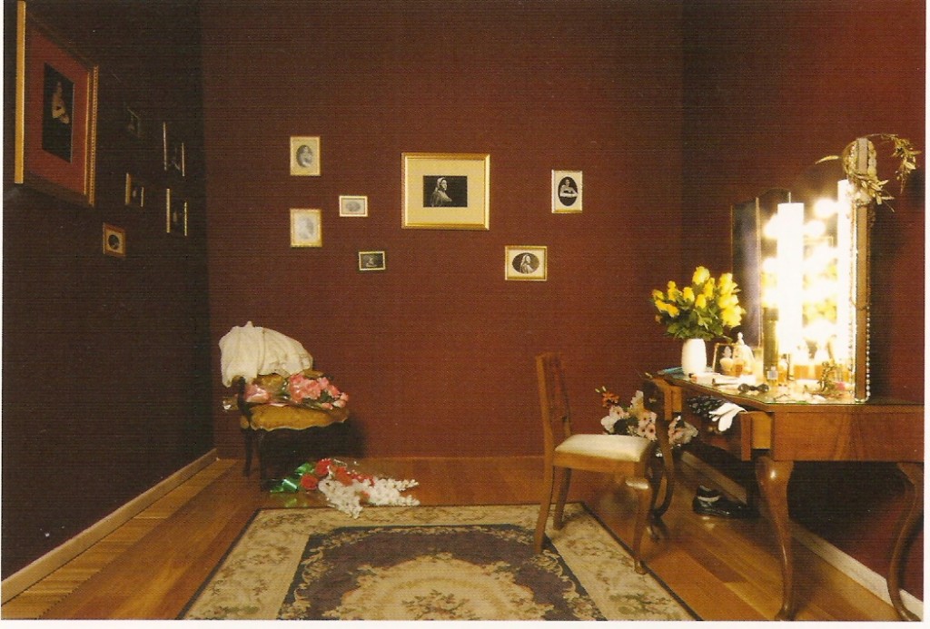 Tocador, cadeiras, cabide, peças de vestuário, adereços, 
 flores e fotografias a preto e branco, dimensões variáveis